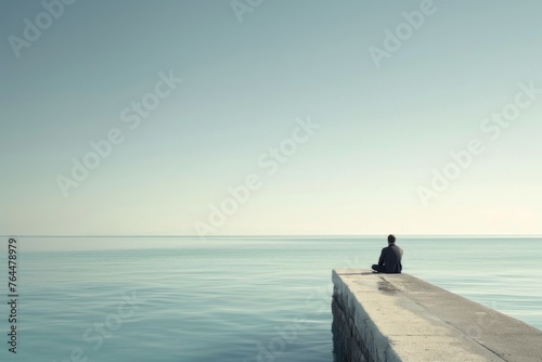 A solitary individual sits at the end of a pier, gazing out at a peaceful sea, lost in contemplation under a clear sky.