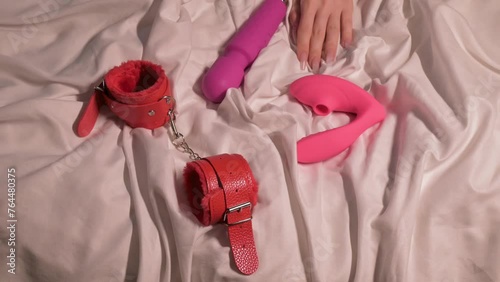 female hand with a set of sex toys for single masturbation and satisfaction on a white sheet on bed. Vibrator, vacuum stimulator and BDSM handcuffs in hand woman girl nymphomaniac photo