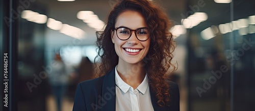 A happy woman wearing glasses is standing in front of a transparent glass wall