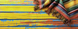 Mexican rug  a serape  for Cinco de Mayo holiday party celebration on bright yellow orange old 
  wooden background, top view, copy space. Fifth of May celebration concept.
