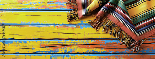 Mexican rug a serape for Cinco de Mayo holiday party celebration on bright yellow orange old wooden background, top view, copy space. Fifth of May celebration concept.