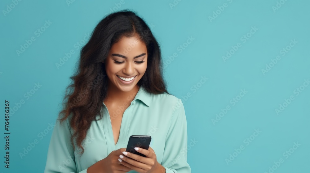 Young adult smiling happy pretty latin woman holding mobile phone looking at smartphone, typing message doing ecommerce shopping on cell, using trendy apps on cellphone isolated on blue background Young adult smiling happy pretty latin woman holding mobile phone looking at smartphone, typing message doing ecommerce shopping on cell, using trendy apps on cellphone isolated on blue background