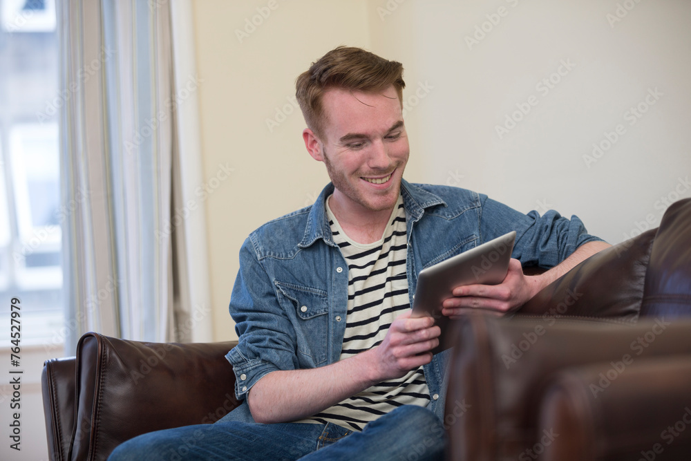 Caucasian man using digital tablet at home on sofa.