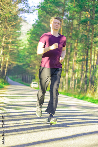 Running man jogging in city park at beautiful summer day. Sport fitness model caucasian ethnicity training outdoor.