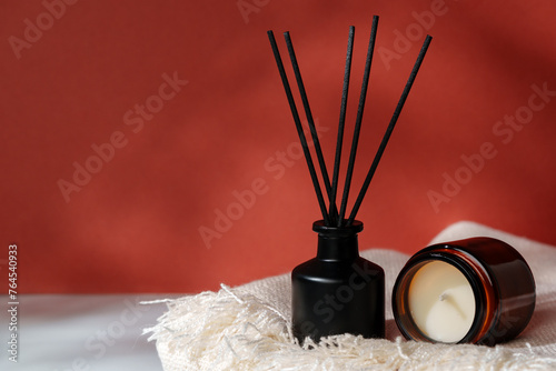 Aromatic Reed Diffuser and Scented Candle on a Woven Mat Against a Warm Red Background