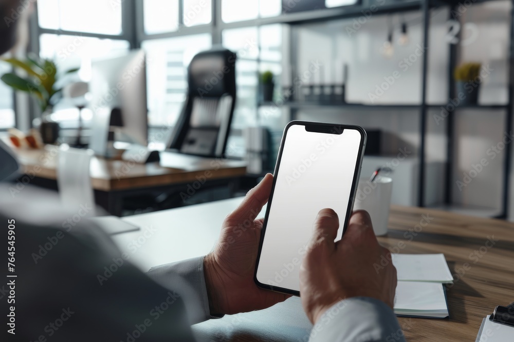 Cropped close-up shot of businessman using smartphone with blank screen while sitting at modern office desk 