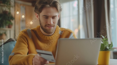 Young adult using a laptop and holding a credit card, conceptualizing online shopping.