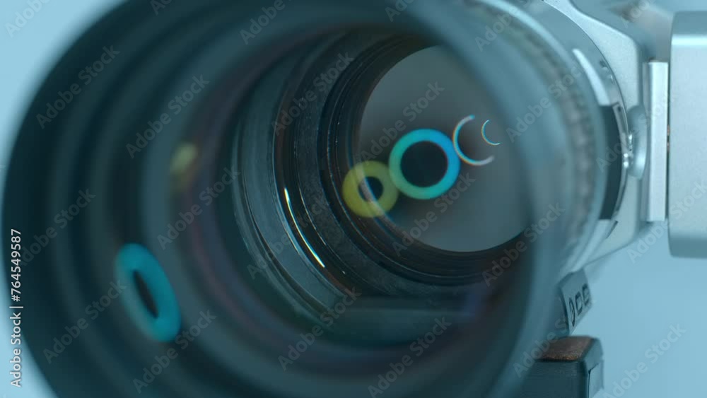 In the studio, ring LED light is reflected in a powerful zoom lens of a professional video camera standing on a tripod against a light background. Closeup. Macro. Shot in motion