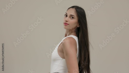 A brunette girl with long straight hair poses in the studio against a light background.