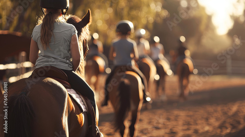 A line of equestrians on horseback enjoys a riding session in an outdoor arena, with the golden sunlight casting a warm glow