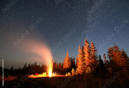 Night camping under starry sky in mountains near forest. Tourists having a rest near campfire under amazing sky full of stars. Camping in Carpathian mountains.