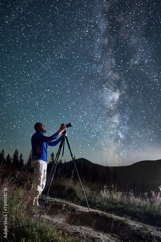 Professional photographer taking photos of Milky Way. Young male focusing his camera to take perfect picture of starry sky. Male taking pictures of night sky full of stars in mountains. © anatoliy_gleb