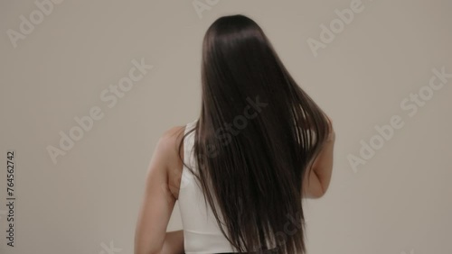 Brunette girl with long straight hair, rear view in the studio on a light background.