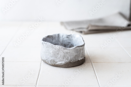 An empty ceramic bowl made of gray clay on a white table against a background of a linen napkin. Horizontal orientation.
