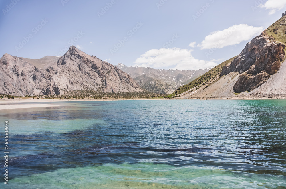 Blue turquoise lake Kulikalon against the backdrop of rocky mountains with glaciers on a warm sunny morning in the Fan Mountains in Tajikistan, landscape in the mountains