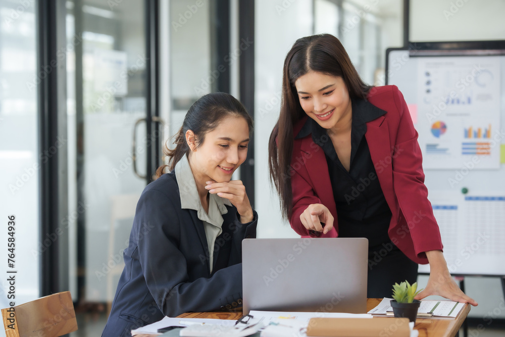 Two women are sitting at a desk looking at a laptop Two women are sitting at a desk looking at a laptop