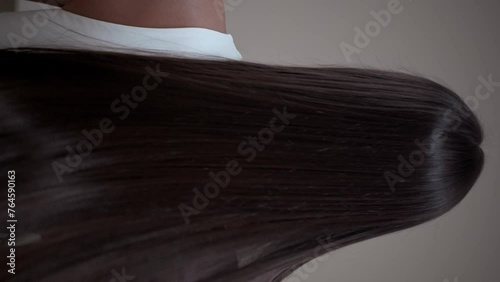 Brunette girl with long straight hair, rear view in the studio on a light background. Vertical video.
