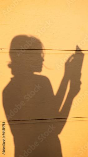 Shadow silhouette of a young woman reading book in morning sunlight. Shade of a girl on a house wall outside. Concept of rest, relax, peace, reading, home, lifestyle, aesthetic, freedom, education.