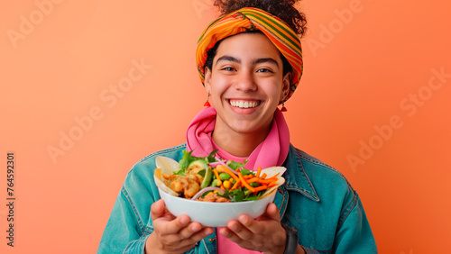 Mexican young woman smiling while holding a plate with mexican food over a peachy background with copy space.