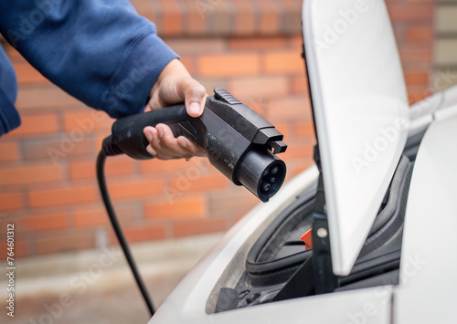 Hand of a woman holding an electric car charger, ready to connect to electric vehicle in front the home.