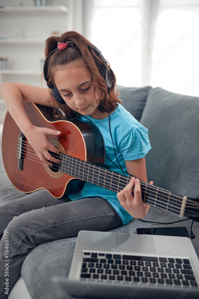Fototapeta premium Kid playing guitar and watching video lessons on a laptop.