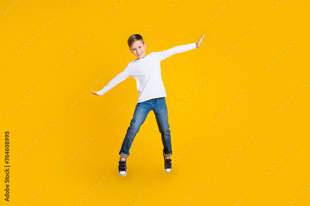 Full length photo of excited good mood boy wear white shirt jumping high flying empty space isolated yellow color background