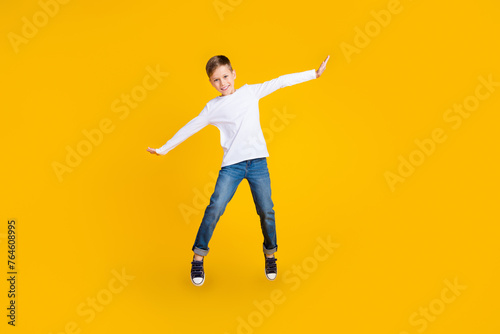 Full length photo of excited good mood boy wear white shirt jumping high flying empty space isolated yellow color background