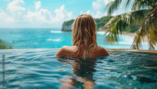 back view young adult female person enjoy relax in infinity edge luxury outdoor swimming pool looking on ocean view in warm sunset light. Tropical wellness travel vacation tourism concept
