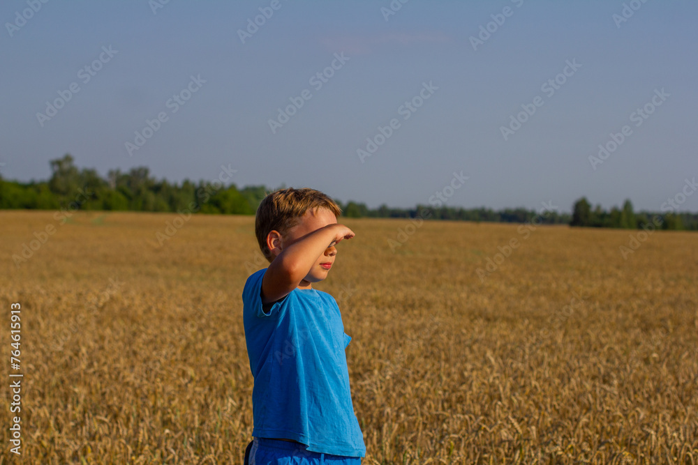 In a wheat field on a summer day, a child looks into the distance, covering his eyes with his hand. Shielding his eyes from the bright summer sun, the child looks at the wheat field. In a wheat field on a summer day, a child looks into the distance, covering his eyes with his hand. Shielding his eyes from the bright summer sun, the child looks at the wheat field.