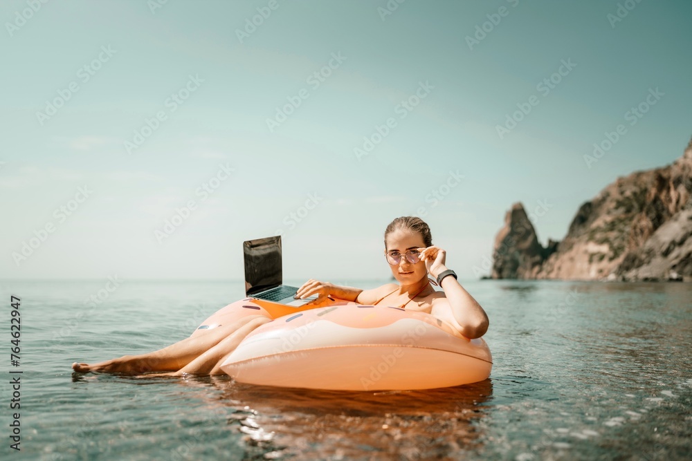 Woman laptop sea. Freelancer woman in sunglases floating on an inflatable big pink donut with a laptop in the sea. People summer vacation rest lifestyle concept