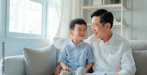 Obraz na płótnie Portrait of father and son. Asian middle age male with boy, smiling and happy sitting indoor. Father's Day concept. w salonie