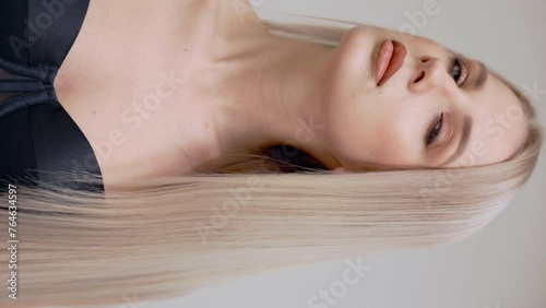 A blonde girl combs her chic long straight hair in the studio on a light background.