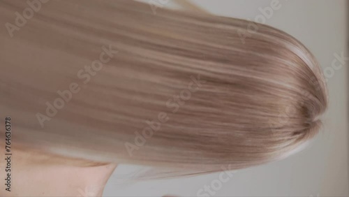 Back view of a blonde girl with long straight hair in the studio. Vertical video.