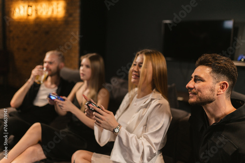Friends observe young women playing console in game room. Content men watch as young ladies adeptly handles challenges with finesse