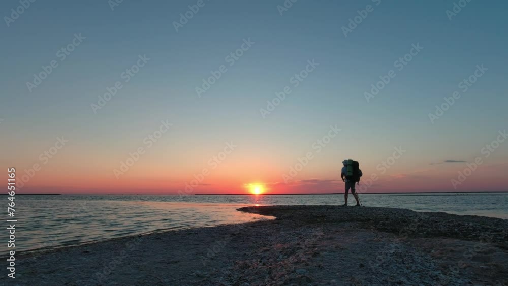 A tourist takes off his backpack against the backdrop of sunrise on the seashore A tourist takes off his backpack against the backdrop of sunrise on the seashore