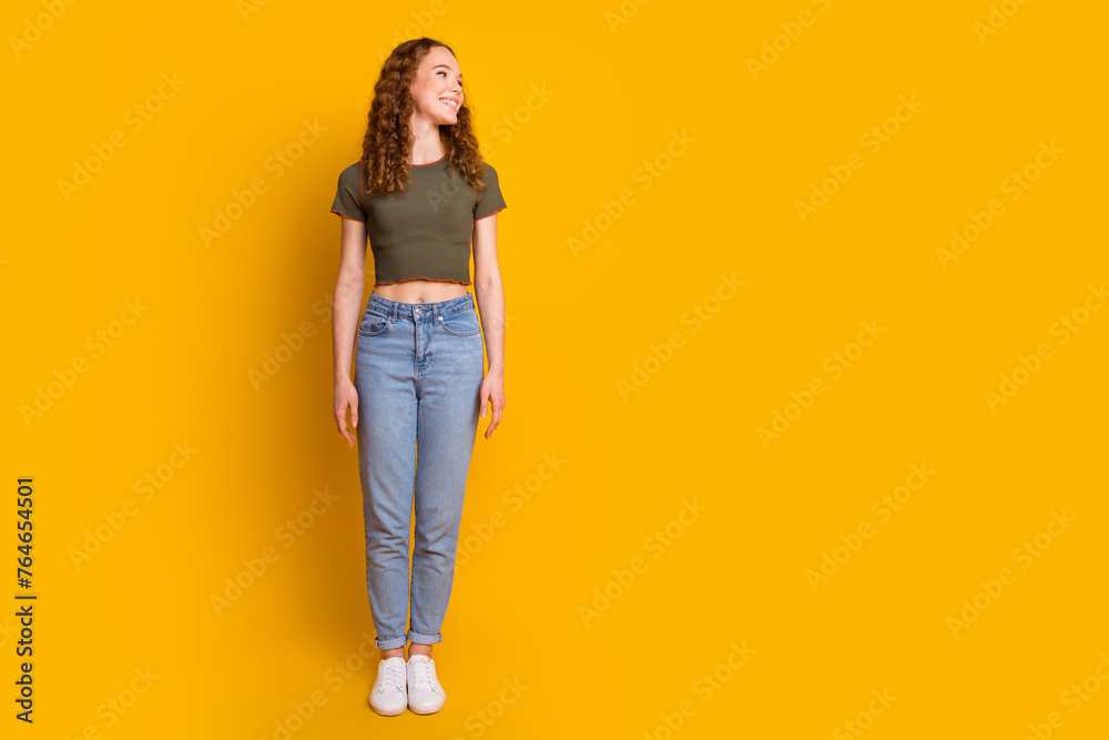 Full length photo of adorable lovely girl dressed stylish clothes looking empty space information isolated on yellow color background