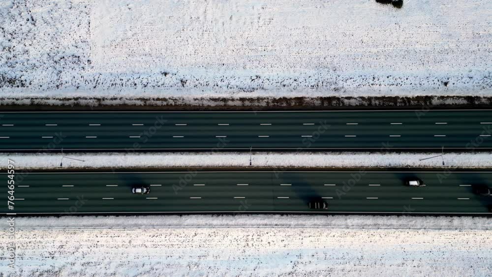 Scenic aerial view of a multi-lane highway, partially plowed and lined with snow-covered evergreen trees, with a few cars traveling along the road in a winter wonderland Scenic aerial view of a multi-lane highway, partially plowed and lined with snow-covered evergreen trees, with a few cars traveling along the road in a winter wonderland