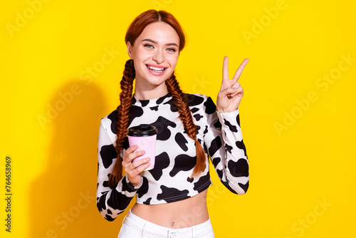 Photo of good mood funky lady dressed cowskin print top showing v-sign enjoying tea isolated yellow color background © deagreez