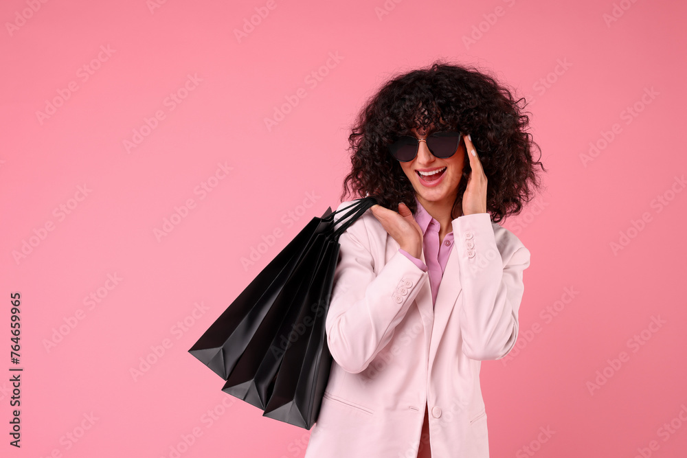 Happy young woman with shopping bags and stylish sunglasses on pink background. Space for text Happy young woman with shopping bags and stylish sunglasses on pink background. Space for text