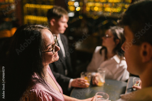 Brunette girl smiles at boyfriend against backdrop of dimmed bar with lamp lighting. Couples on double date in favorite pub