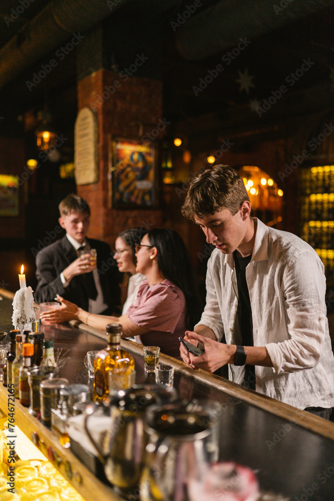 Guy in wrinkled shirt holds smartphone standing at counter in bar. Drunk man with mobile device at party in fancy nightclub