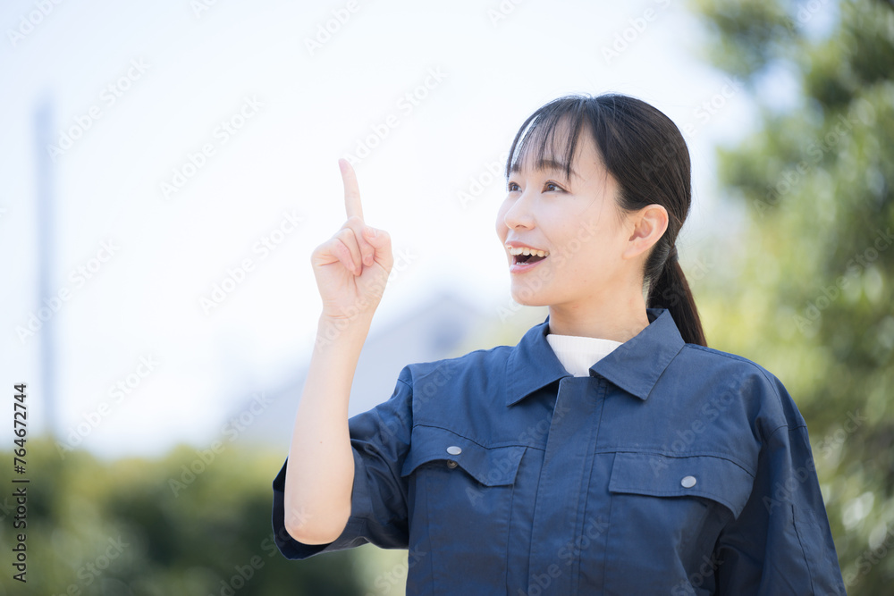 新緑の青空の屋外で作業着を着た女性　ポイントの指差しの横顔