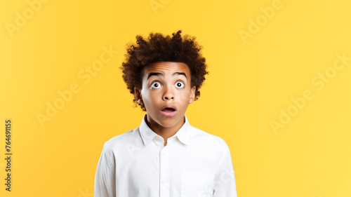Photo of astonished boy with curly hair dressed white shirt staring at empty space isolated on yellow color background. 