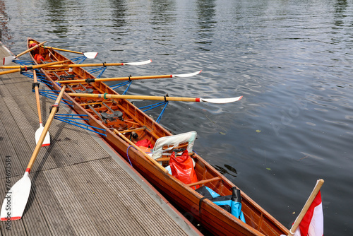 Ein Ruderboot, Mehrsitzer hat an einem Steg an einem Boothaus fest gemacht.
 photo