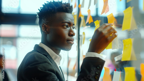 A man in a jacket is placing sticky notes on a glass wall.