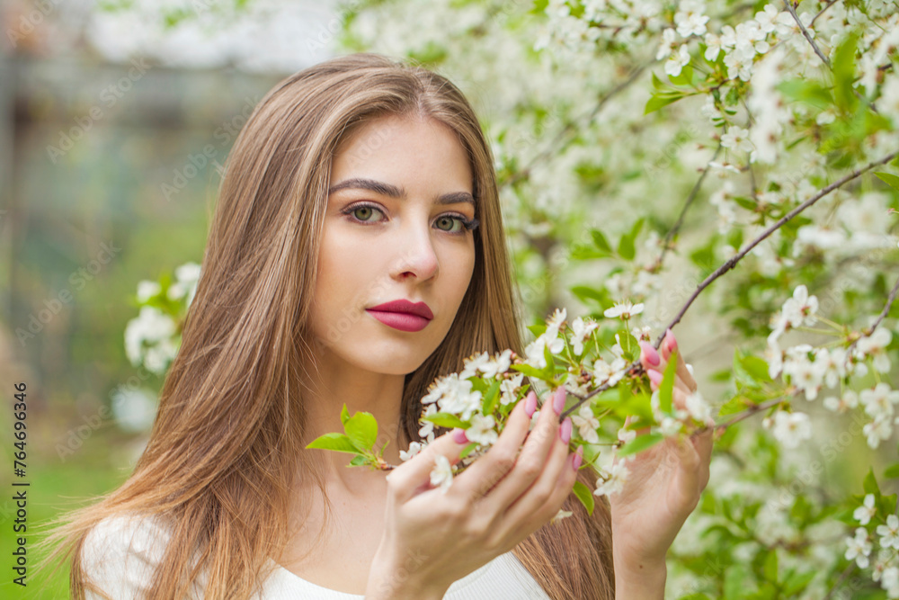 Fototapeta premium Fashion portrait of young woman with natural makeup and healthy long brown hair in blossom park outdoors. Natural female beauty