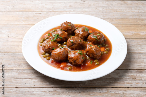 Meatballs, green peas and carrot with tomato sauce isolated on white background on wooden table
