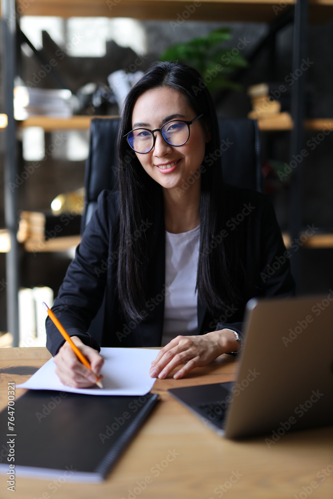In her office, a young woman, an entrepreneur, writes diligently on her laptop, embodying professionalism and dedication.