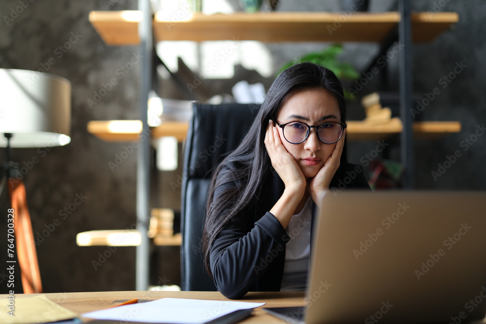 A tired Korean businesswoman looks stressed and exhausted while working on her laptop in the office.
