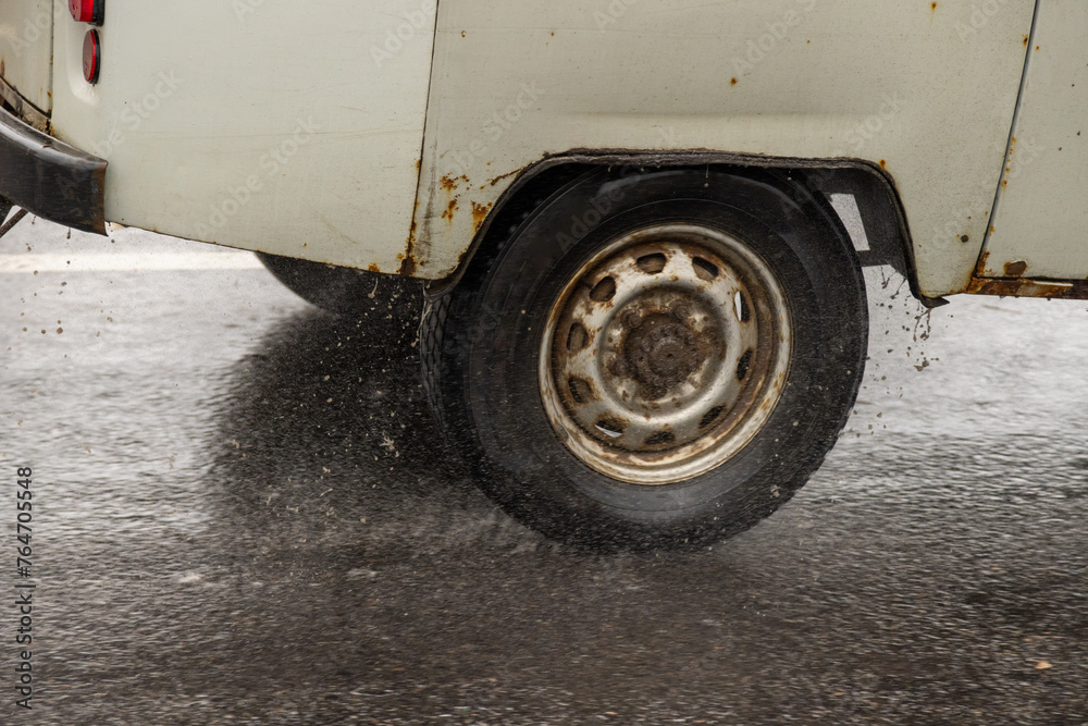 old rusty soviet minivan driving on the wet asphalt road during heavy rain.